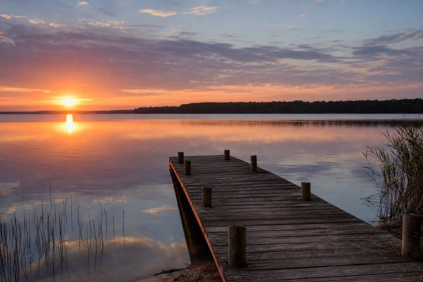 Ponton en bois sur le lac de Biscarrosse-Parentis au coucher du soleil, rive de pins à l'horizon